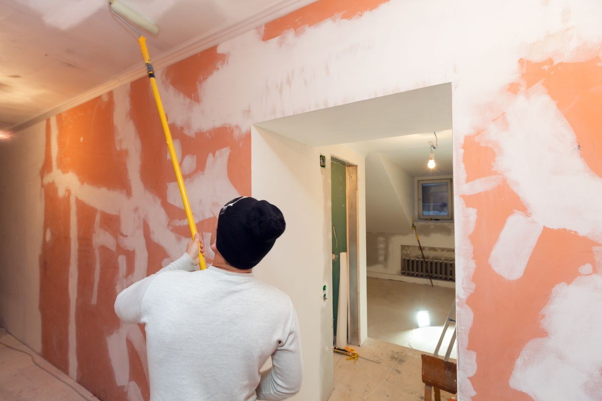 Worker is painting the ceiling by paint roller in corridor an apartment is inder construction, remodeling, renovation, overhaul, extension, restoration and reconstruction. Concept of home improvement